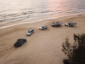 Five vehicles on a beach, each of the vehicles has a different Outbound awning mounted.